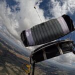Deployed ram-air parachute and pilot chute above fields