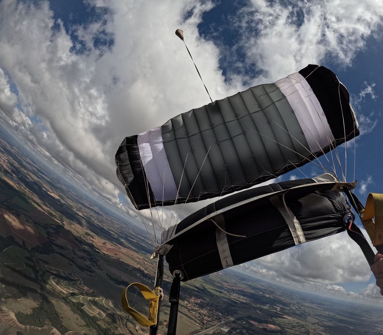 Deployed ram-air parachute and pilot chute above fields