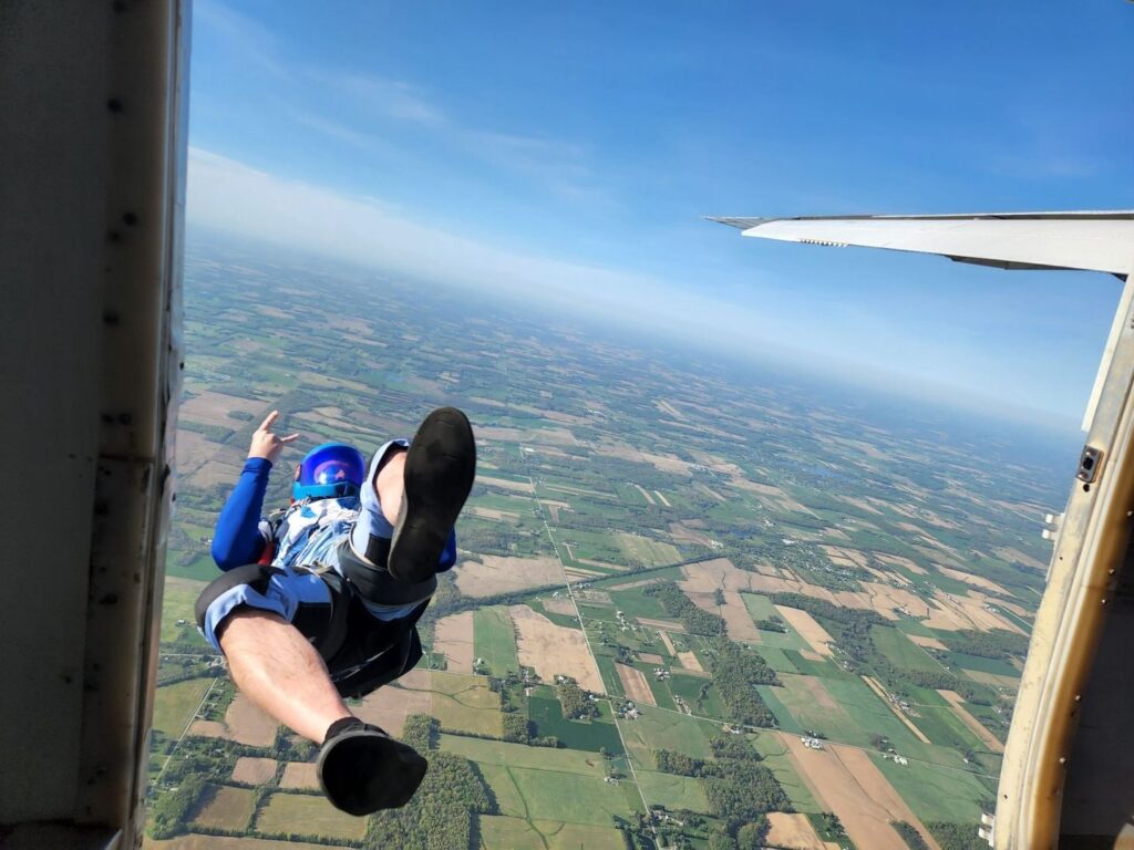 Skydiver exits an aircraft above a patchwork of farmland