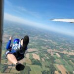 Skydiver exits an aircraft above a patchwork of farmland