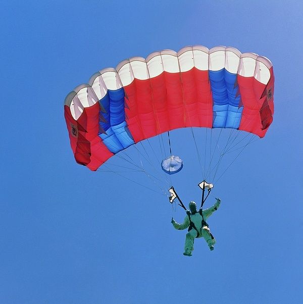 Parachutist suspended beneath a partially inflated red, white, and blue canopy