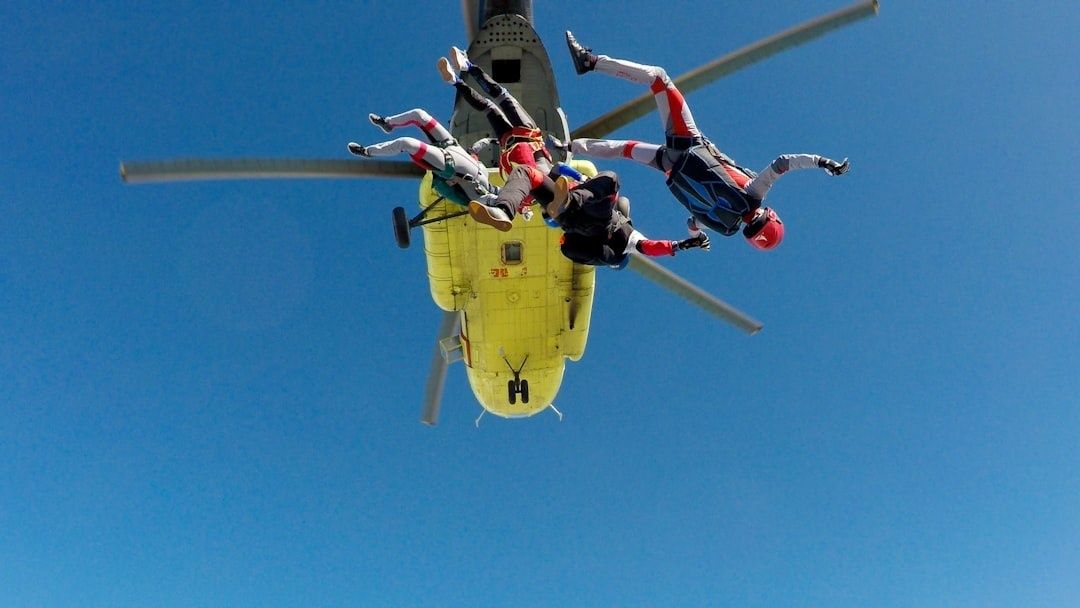 Skydivers exit a yellow helicopter against a clear blue sky