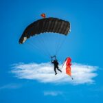 Skydiver descending beneath a black parachute against a blue sky