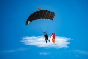 Skydiver descending beneath a black parachute against a blue sky
